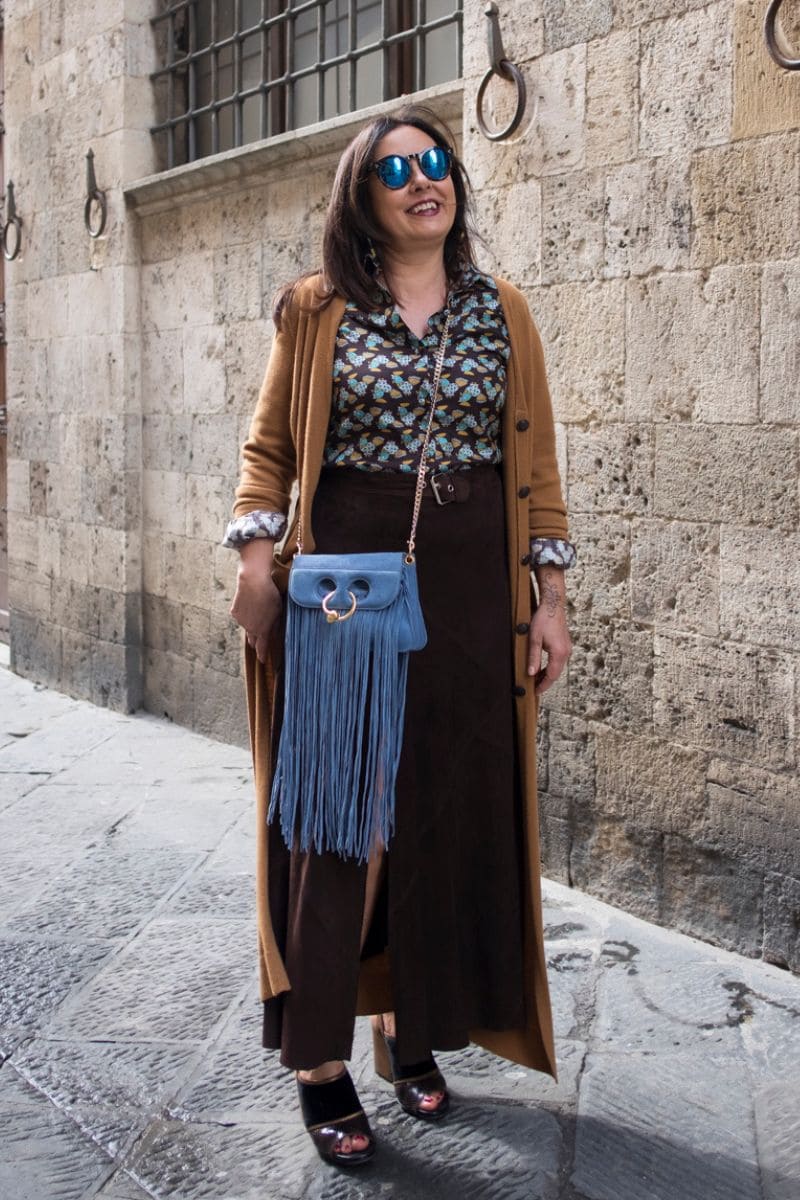 Donna over 60 con gonna marrone e borsa azzurra, abbinamento fresco e luminoso