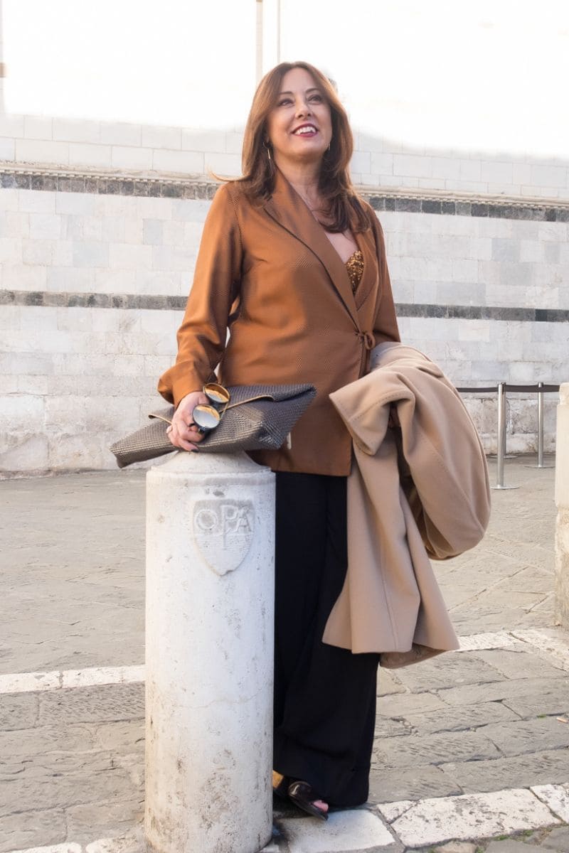Donna over 60 con cappotto cammello e pantaloni neri, abbinamento marrone con nero chic e moderno